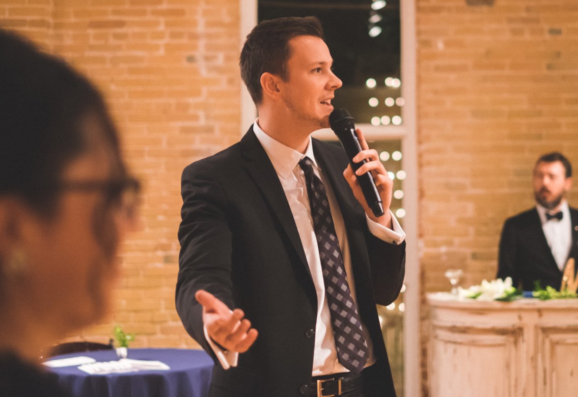 A Tully Entertainment host in a suit, microphone in hand, speaking to wedding guests